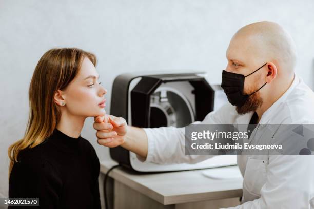 bold male doc in black medical mask talking with female patient in the cabinet - dermatologists talking to each other patient stock pictures, royalty-free photos & images