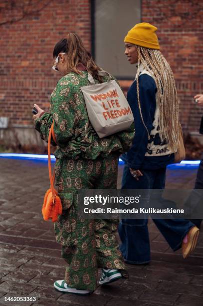 Guest wearing navy blue wide jeans, navy blue denim jacket, brown bag, and yellow hat, and a guest wearing army green pants with a brown pattern and...