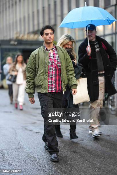 Guest wears a green pearls necklace, a white tank-top, a red and black / white checkered print pattern shirt, black cargo pants, black shiny leather...