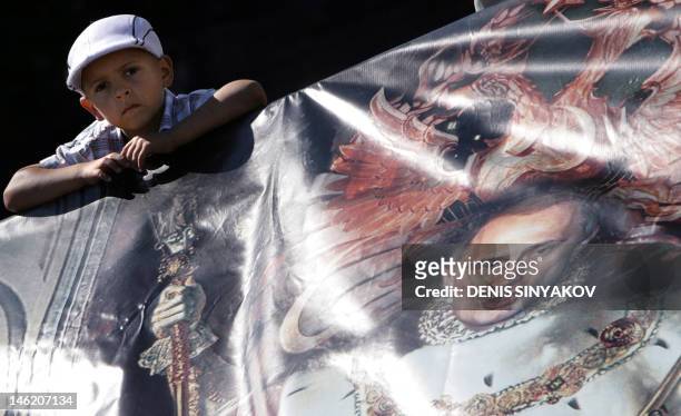 Boy sits behind a banner showing Russian President Vladimir Putin at the anti-globalization tent camp set up at the Kirov stadium in St.Petersburg,...