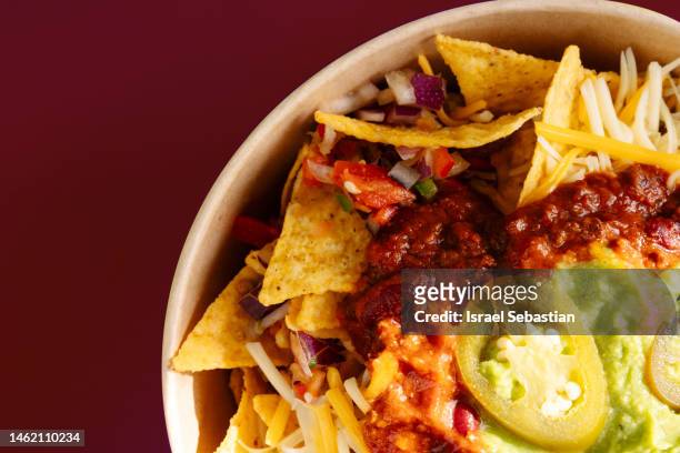 close-up view of a plate of nachos, traditional mexican food, on a plain maroon background. - nachos stock pictures, royalty-free photos & images