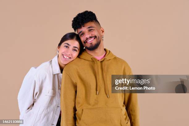 middle shot of a couple of friends smiling and looking at the camera in a brown studio background - couple studio stock pictures, royalty-free photos & images