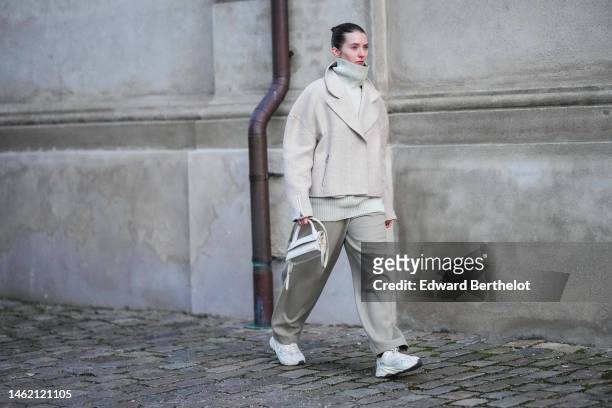 Guest wears a beige ribbed wool turtleneck pullover, a beige wool oversized jacket, beige suit pants, a white matte leather handbag from Jacquemus,...