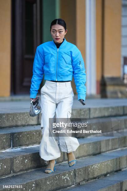 Guest wears a black turtleneck pullover, a blue nylon cropped bomber coat, white cargo puffy pants, a silver shiny varnished leather handbag, beige...