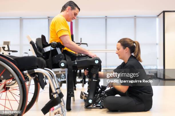 mechanical exoskeleton. physiotherapy in a modern hospital: physiotherapist woman helping with the tapes to the disabled person with the robotic skeleton. scientists, engineers and physiotherapy rehabilitation doctors use a tablet to help - fake hospital stock-fotos und bilder