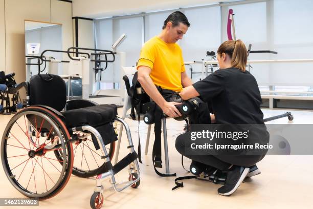 mechanical exoskeleton. physiotherapy in a modern hospital: female physiotherapist placing the tapes on the disabled person to put on his robotic skeleton. scientists, engineers and physiotherapy rehabilitation doctors use a tablet to help - fake hospital stock-fotos und bilder