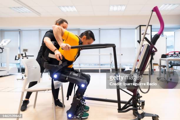 mechanical exoskeleton. physiotherapy in a modern hospital: physiotherapist helping to get up the disabled person with the robotic skeleton. scientists, engineers and physiotherapy rehabilitation doctors use a tablet to help - hospital machine stockfoto's en -beelden