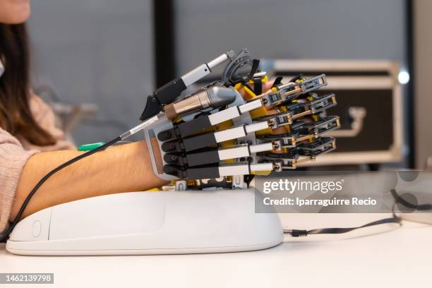 mechanical exoskeleton hand. physiotherapy in a modern hospital: female patient in rehabilitation exercises with the mechanical hand, looking at the computer. scientists, engineers and physiotherapy rehabilitation doctors use a tablet to help - esoscheletro di animale foto e immagini stock