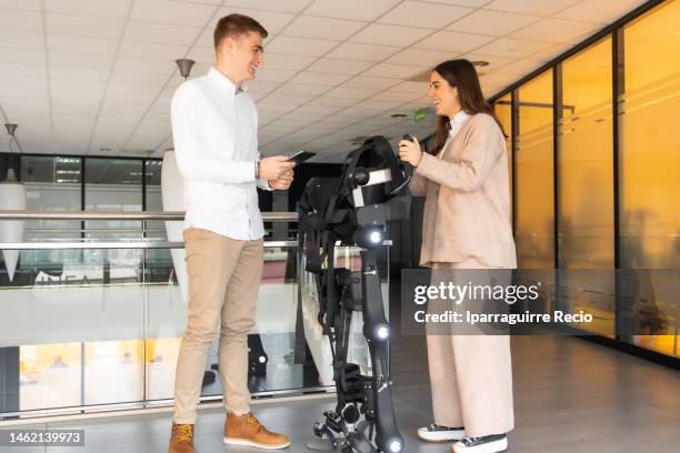 mechanical exoskeleton. physiotherapy in a modern hospital: physiotherapist and scientist talking and preparing the robotic skeleton outside the rehabilitation box. scientists, engineers and physiotherapy rehabilitation doctors use a tablet to help - animal exoskeleton stock pictures, royalty-free photos & images