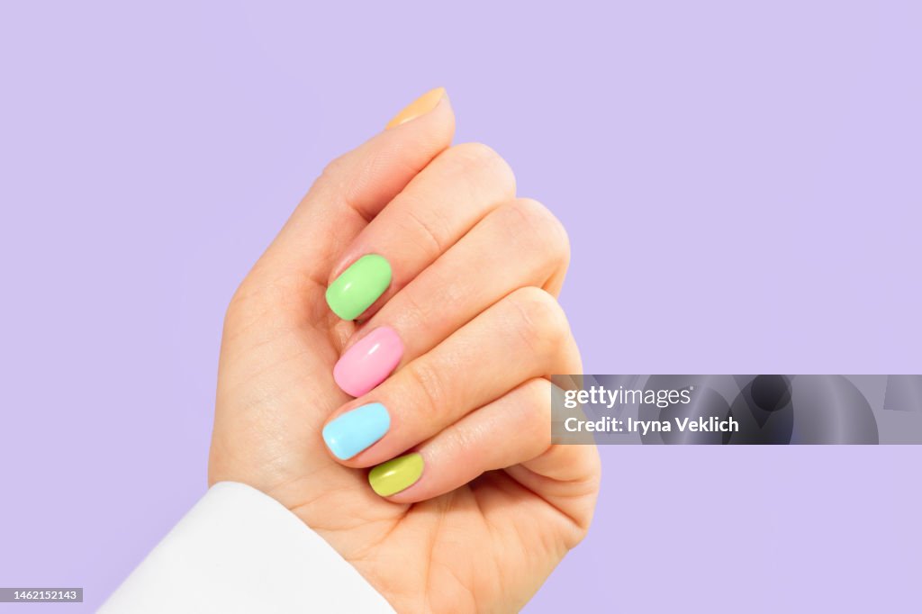 Elegant woman's hand with pastel color manicure on Easter Holiday. Trendy Color of the Year 2022 Very Peri purple violet lavender color background. Woman dressed in fashionable white shirt.