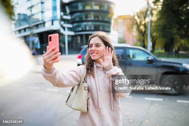 beautiful middle-aged woman with long hair in tracksuit with smartphone on street of city near road. - one woman only videos stock pictures, royalty-free photos & images