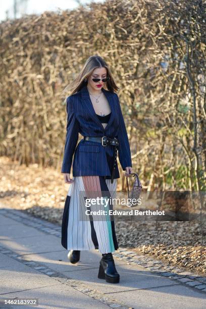 Guest wears black sunglasses, silver earrings, a silver large chain necklace, a black V-neck / cropped top, a navy blue striped print pattern blazer...