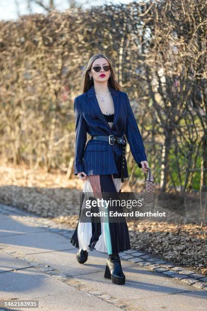 Guest wears black sunglasses, silver earrings, a silver large chain necklace, a black V-neck / cropped top, a navy blue striped print pattern blazer...