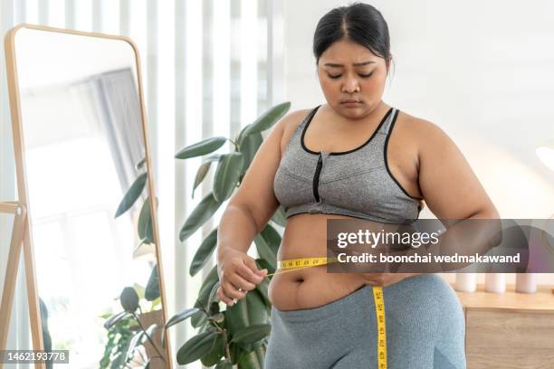 nice chubby woman measuring her waist while standing in front of the mirror - taille stockfoto's en -beelden