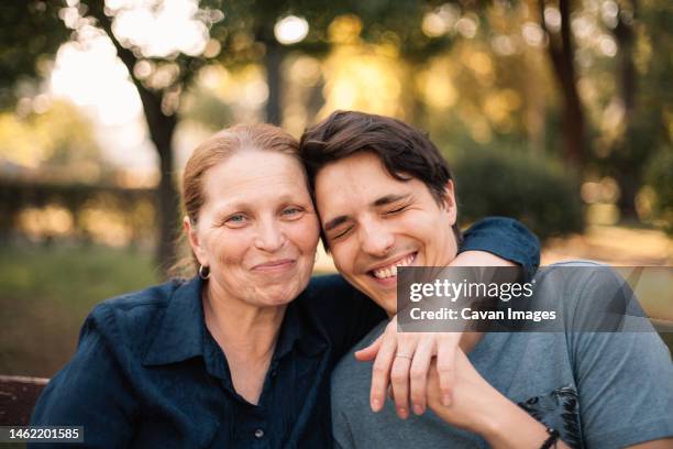 happy mature mother hugging smiling adult son in park in summer - mutter sohn erwachsen stock-fotos und bilder