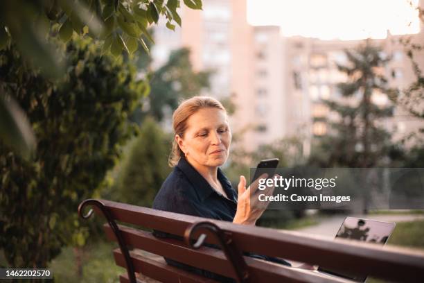 happy mature business woman using smart phone and laptop in park - ukraine people stock pictures, royalty-free photos & images
