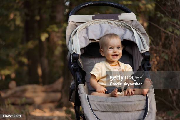 happy baby girl sitting in stroller at the park. - baby stroller imagens e fotografias de stock