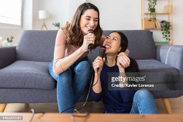 multiracial young women laughing having fun playing karaoke together at home. female friendship concept - karaoke anlage stock-fotos und bilder