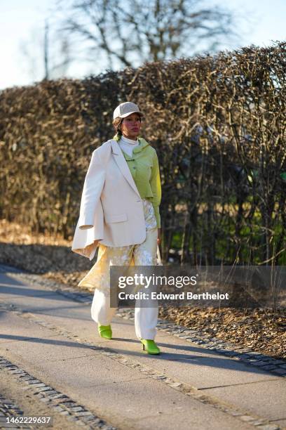 Guest wears a beige cap from Munthe, gold earrings, a white latte turtleneck pullover, a green nylon jacket, a beige blazer jacket, a pale yellow and...