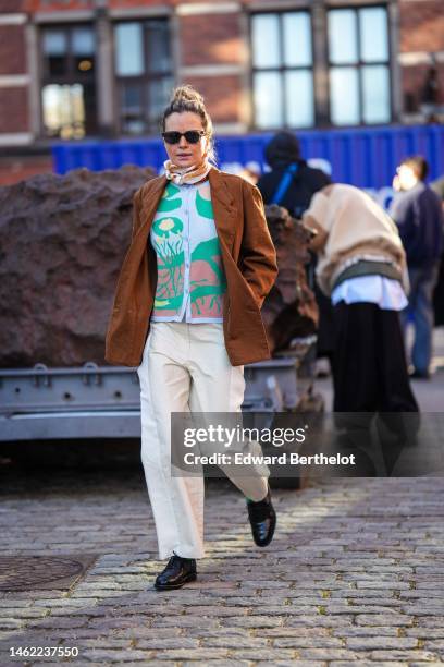 Guest wears brown sunglasses, a white and brown print pattern silk scarf, a pale gray with green and yellow leaves buttoned wool cardigan, a brown...