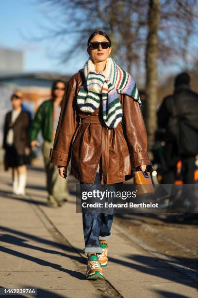 Guest wears black sunglasses, a white with green / blue / pink striped print pattern wool oversized pullover, a dark brown shiny leather belt coat,...