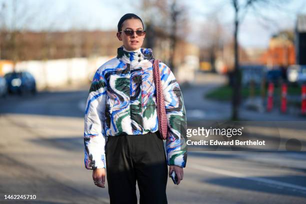 Guest wears brown sunglasses, a white with black / green / blue / pink print pattern high neck puffer jacket, a pink braided shiny leather shoulder...