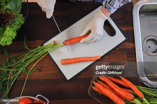 seguridad alimentaria - corte de zanahorias en tabla de cortar de plástico con guantes de comida - tabla de cortar fotografías e imágenes de stock