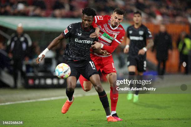 Edmond Tapsoba of Bayer 04 Leverkusen runs with the ball whilst under pressure from Mergim Berisha of FC Augsburg during the Bundesliga match between...