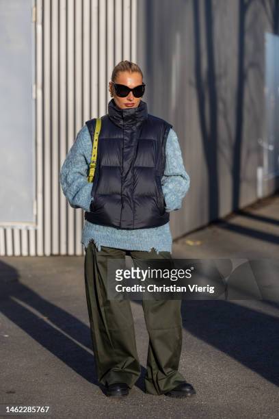 Guest wears navy puffer vest, blue knit, khaki wide leg pants, black boots, sunglasses outside Holzweiler during the Copenhagen Fashion Week...