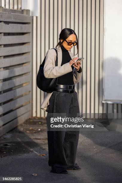 Guest wears wide leg denim jeans, black belt, turtleneck, bag, grey jacketoutside Holzweiler during the Copenhagen Fashion Week Autumn/Winter 2023 on...