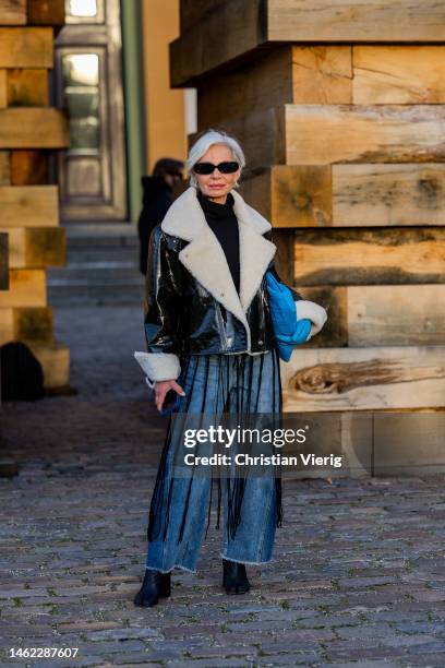 Grece Ghanem wears black white shearling jacket, denim jeans, black ankle boots, blue bag & a guest wears brown leather jacket, denim skirt,...