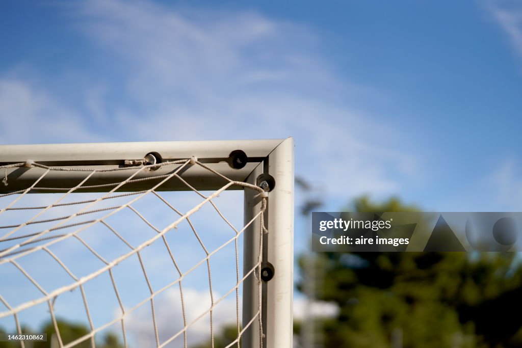 Corner of a metal post on an unmanned soccer field with its netting, rear view with clear sky