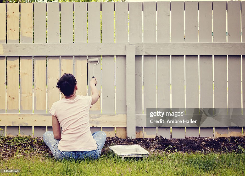 Woman sitting cross legged painting a fence