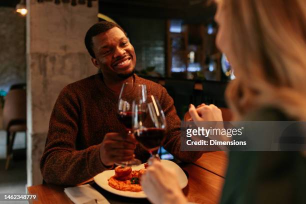 pareja multicultural brindando con vino en restaurante. - mesa para dos fotografías e imágenes de stock