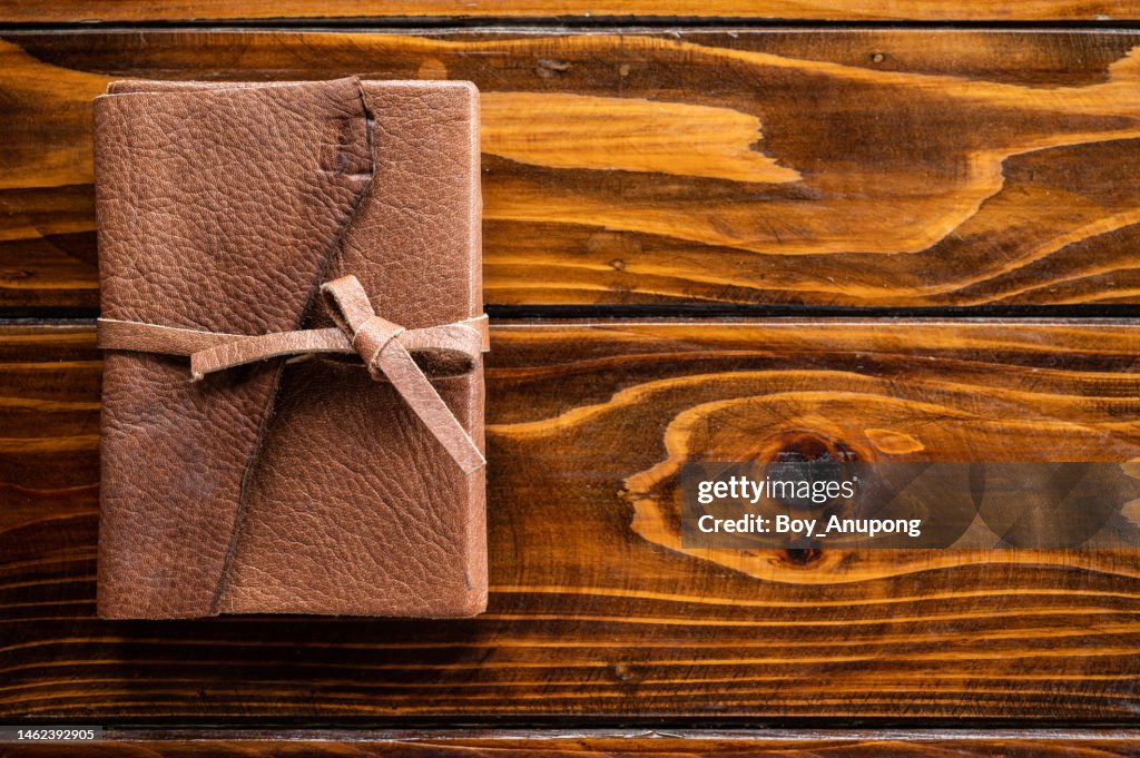 A diary book with leather cover and leather strap on wooden table.