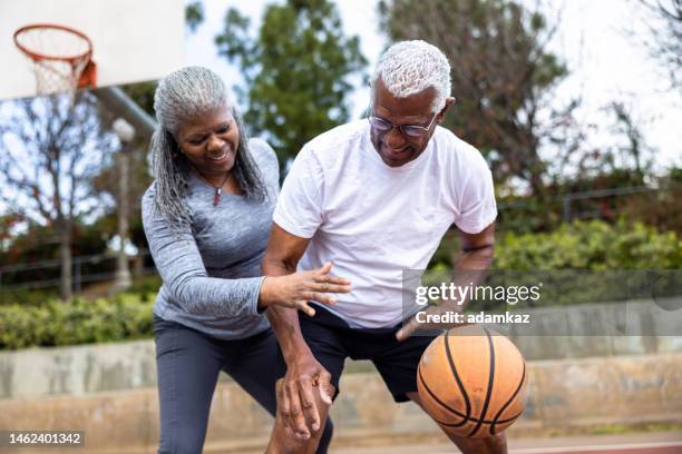 senior black man dribbling basketball while wife defends him - the old guard stock pictures, royalty-free photos & images