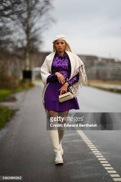 Guest wears a white beret wool hat, silver pendant earrings, a purple sequined high neck / long sleeves / t-shirt, a white latte fringed scarf, a...