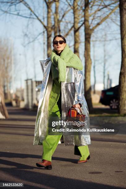 Julia Haghjoo wearing apple green velvet suit, green knitted sweater knotted around the shoulder, long silver coat, brown and red Loewe bag, and...