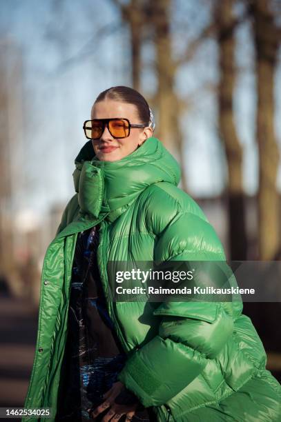Marianne Theodorsen wearing a green long oversized puffer jacket, black striped print pattern wide suit pants, orange sunglasses, and green sneakers...