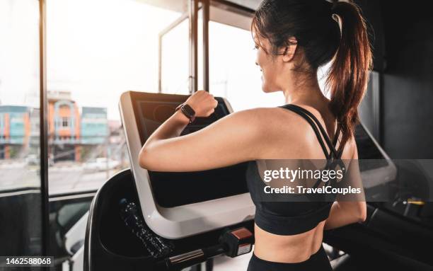 woman running in a gym on a treadmill concept for exercising. fitness and healthy lifestyle. girl running on the treadmill and listening to music at the gym - smart watch on wrist stock pictures, royalty-free photos & images