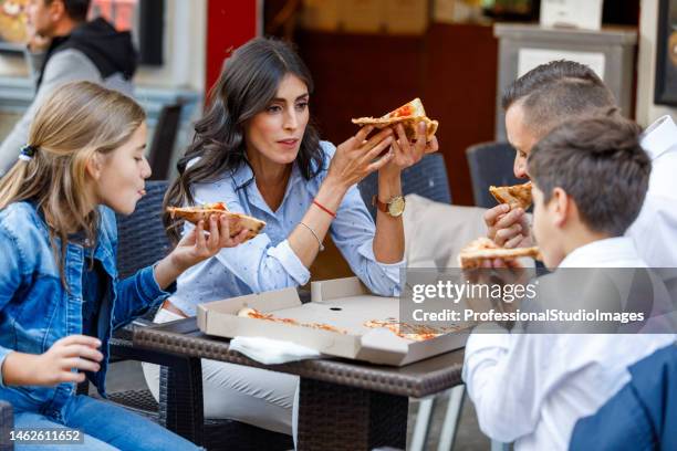 little brother and sister are happy to eat a pizza slice with their parents in the city. - pizza restaurant stock pictures, royalty-free photos & images