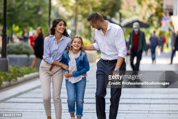 young father and mother are walking through the city streets with a daughter and holding hands together. - street promenade stock pictures, royalty-free photos & images
