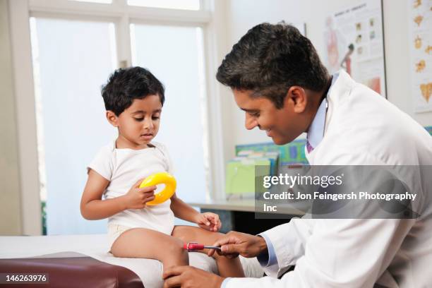 indian doctor testing boy's reflexes in doctor's office - reflex hammer stock pictures, royalty-free photos & images