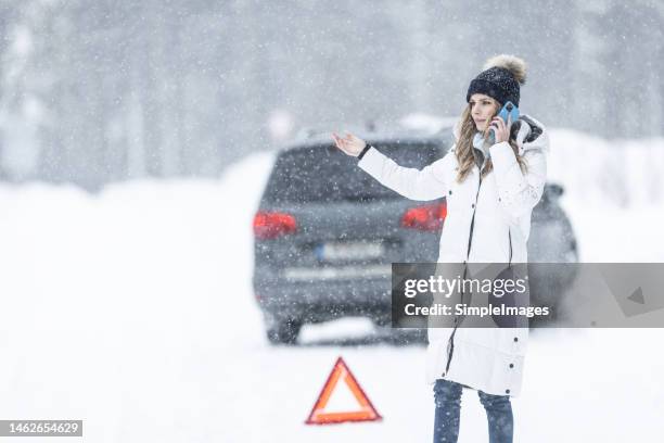 young woman who slid off the road with a minivan calls on the phone for help with emergency triangle out on the road. - winter panne auto stock-fotos und bilder