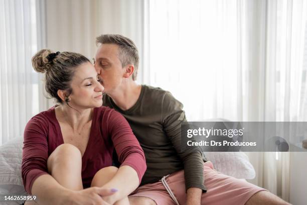 mann küsst seine frau im bett - baby boomer couple stock-fotos und bilder