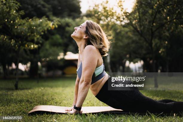 woman practicing physical exercise on mat in public park - 50 54 years stock pictures, royalty-free photos & images