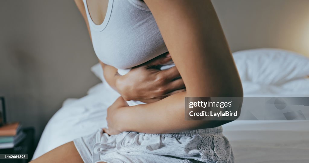 Menstruation, stomach ache and hands of woman in bedroom for indigestion, cramps and illness. Frustrated, gas and stress with girl on bed for constipation, bloating and intestine problems at home