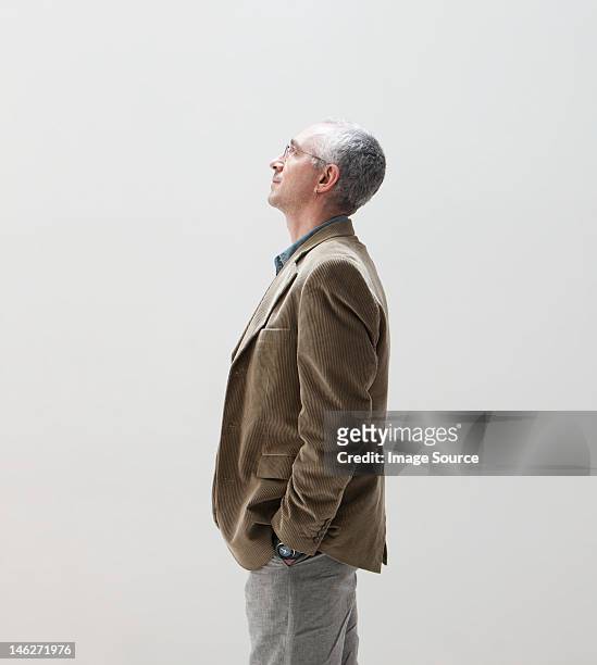 mature man with hands in pocket looking up, studio shot - white jacket 個照片及圖片檔