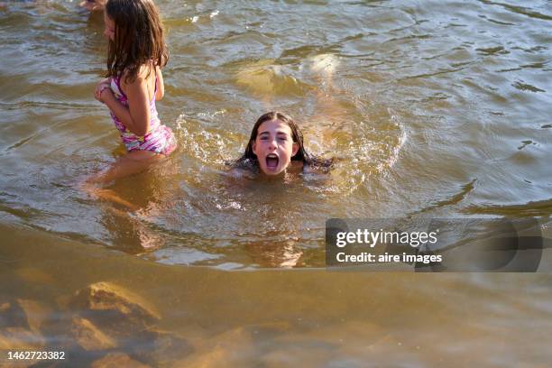 girl swimming in the lake sharing with her siblings, opening her mouth to take in air to dive under the water. - river bathing stock pictures, royalty-free photos & images