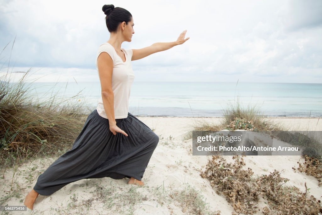 Woman practicing tai chi chuan on beach, side view